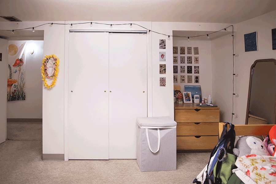 A tidy bedroom closet area with sliding doors, a dresser, string lights, photos on the wall, and a laundry basket.